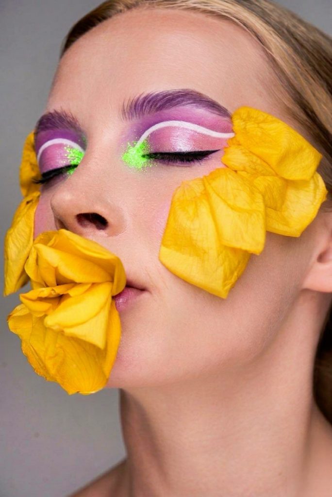 spring beauty editorial story for a fashion magazine. olIVE SKIN MODEL WITH PERFECT SKIN MAKEUP AND ORANGE AND GOLD EYE SHADOWS. Nude LIPS with florals around the face.
